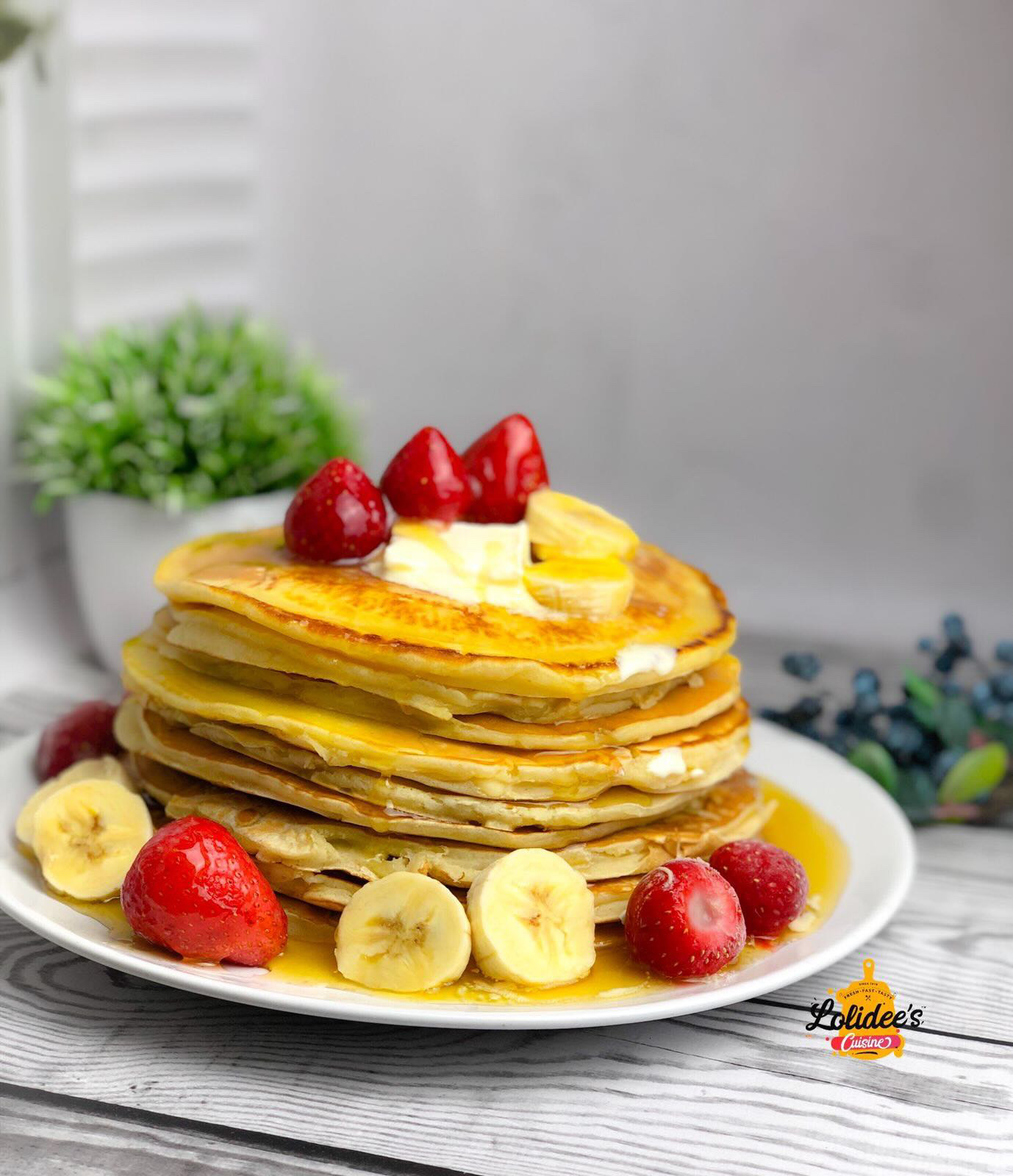 Stack of fluffy pancakes with strawberries, banana and syrup